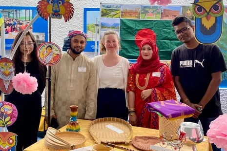 Studierende aus Bangladesch an buntdekoriertem Stand.